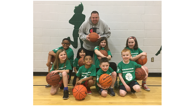 basketball coach and team of kids with basketballs smiling on the court